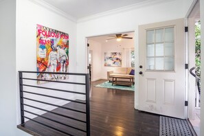 Un couloir avec un portail en métal noir, une porte blanche dotée de panneaux de verre et un ventilateur de plafond.