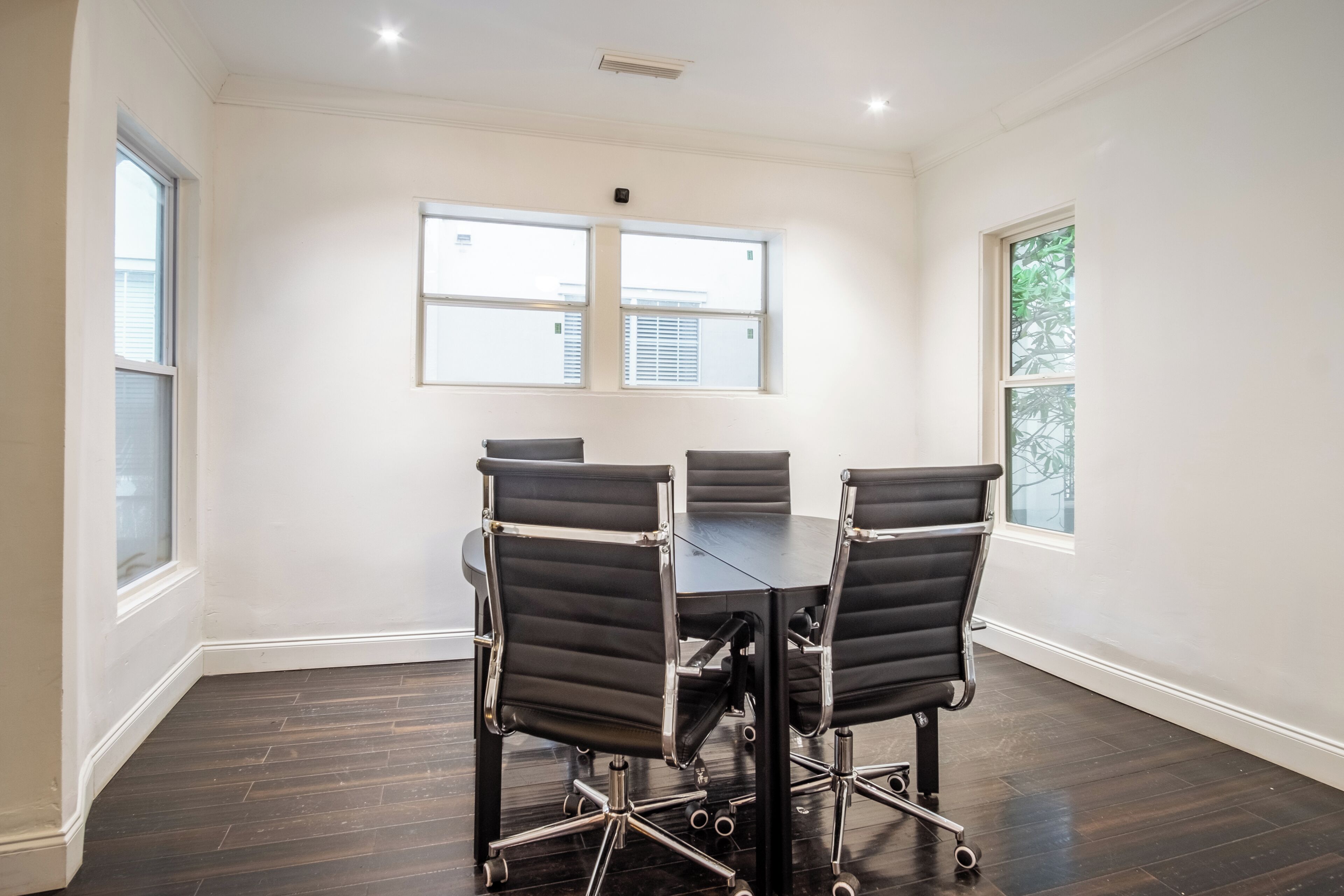 A conference room with a dark wood floor, white walls, and a large table with four chairs.