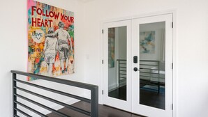 Un couloir avec une porte en verre, un escalier doté d’une rampe en métal et une affiche colorée accrochée au mur.