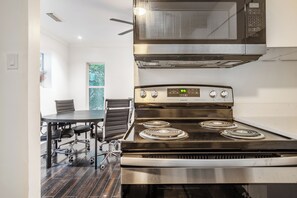 Een moderne keuken met een roestvrijstalen fornuis, een magnetron erboven en een eethoek met een tafel en stoelen.
