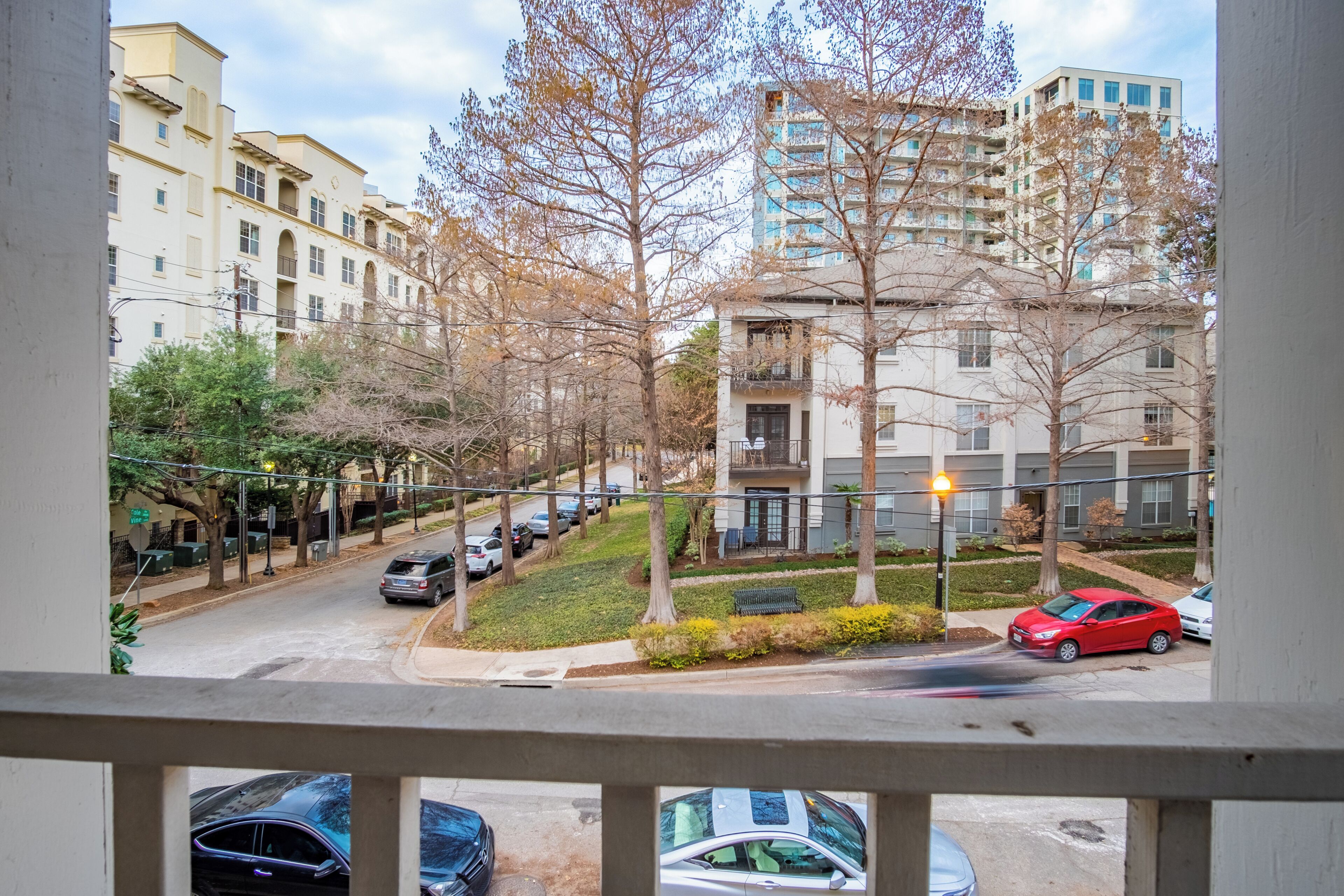 A residential street with parked cars, trees, and multi-story buildings.