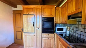 Een keuken met houten kastjes, een koelkast, een oven, een magnetron en een betegelde achterwand.