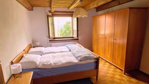 Een slaapkamer met twee bedden, een raam, een houten garderobe en een klein nachtkastje.