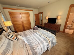 A bedroom with a bed, a dresser, a television, and a bathroom visible through an open door.