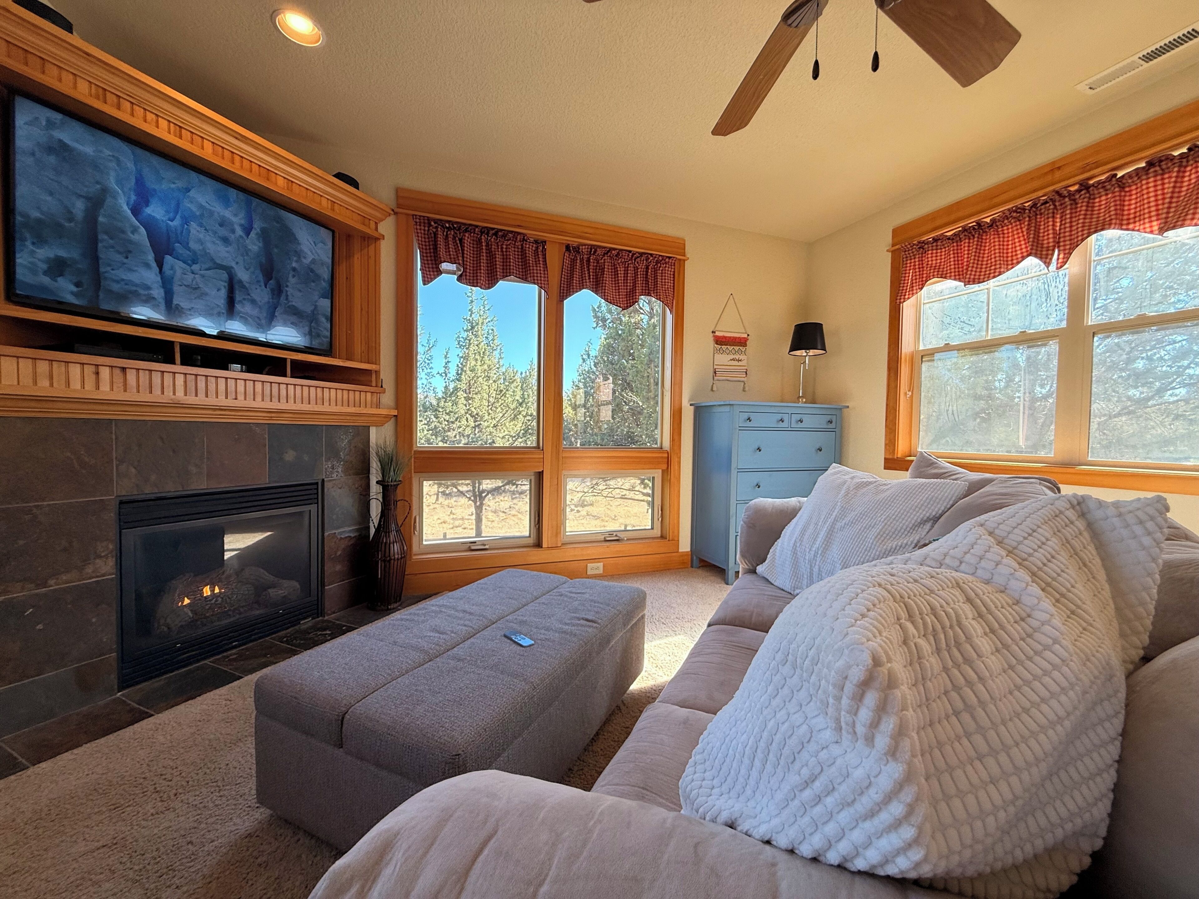 Una sala de estar con chimenea, televisor, sofá y ventanas amplias con cortinas.