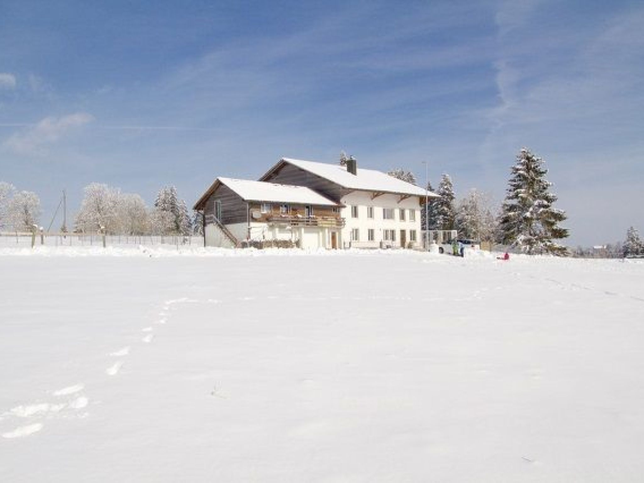 Um edifício grande de dois andares com telhado coberto de neve, cercado por uma paisagem e árvores nevadas.
