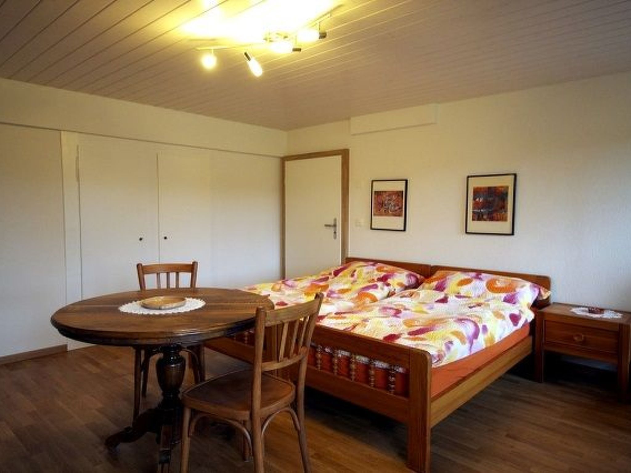 A bedroom with a bed, a wooden chair, a small table, and a nightstand.