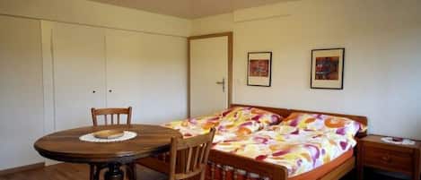 A bedroom with a bed, a wooden chair, a small table, and a nightstand.