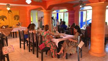 Restaurante com várias mesas e cadeiras, um ventilador de teto e janelas amplas.