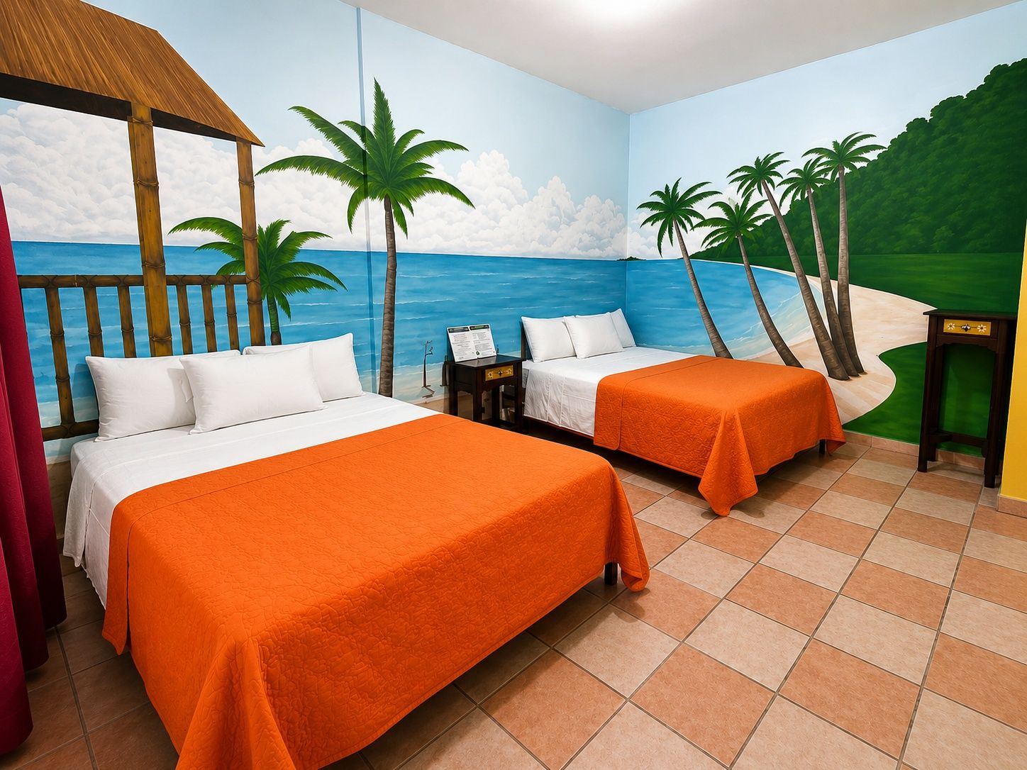 A hotel room with two beds, a wooden headboard, a small table, and a mural of a beach scene.