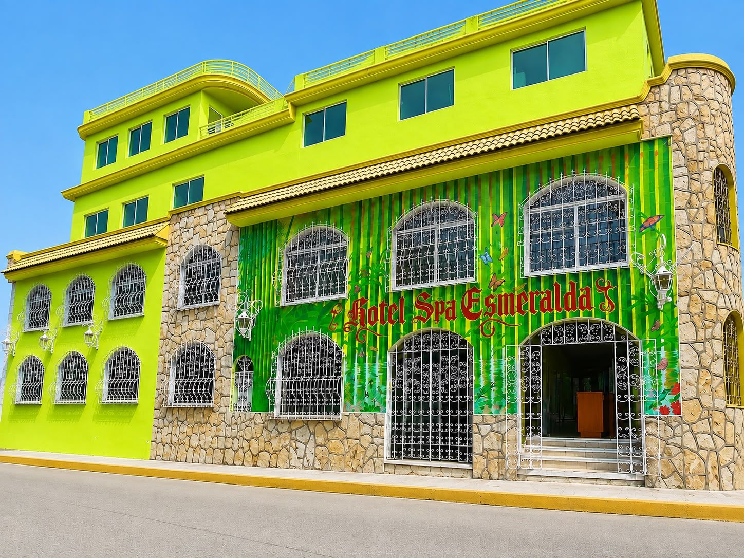 Un edificio de varios pisos con fachada verde brillante y base de piedra, que presenta una gran entrada arqueada y múltiples ventanas con barrotes.
