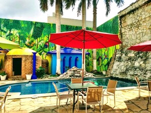 Un área de piscina con mesa y sillas, una sombrilla roja y un muro de piedra.