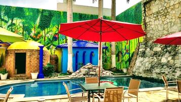 Un área de piscina con mesa y sillas, una sombrilla roja y un muro de piedra.