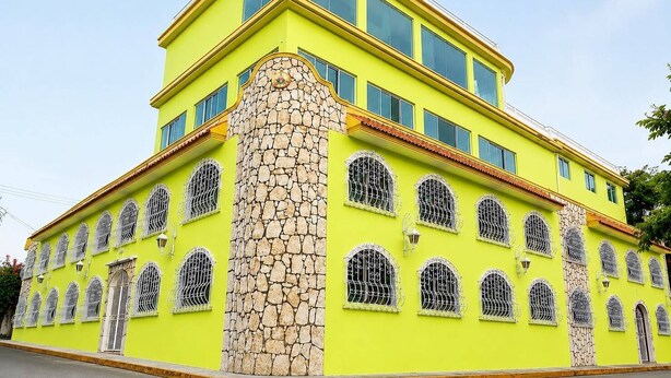 A multi-story building with a yellow facade, multiple windows with metal bars, and a stone column.