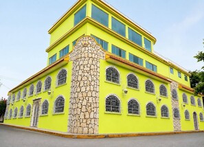 Un edificio de varios pisos con fachada amarilla, numerosas ventanas con barrotes de metal y una columna de piedra.
