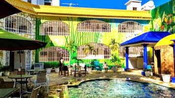Un patio con piscina, mobiliario exterior y un edificio con grandes ventanales y un mural.