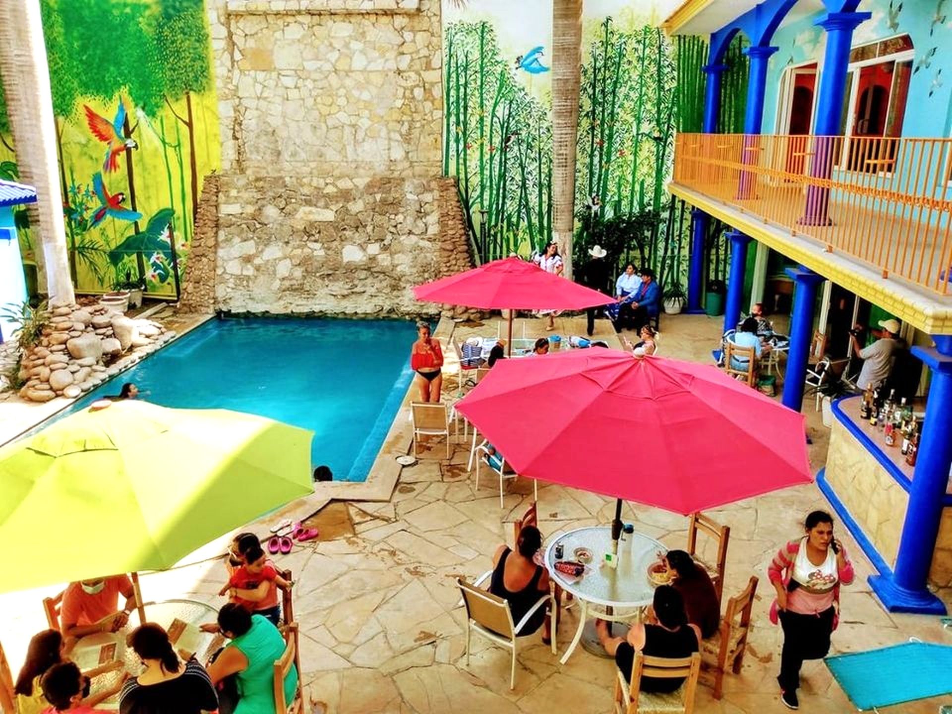 Zona de piscina exterior con paredes de piedra, un mural y un área de bar con pilares azules.