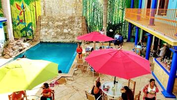Zona de piscina exterior con paredes de piedra, un mural y un área de bar con pilares azules.