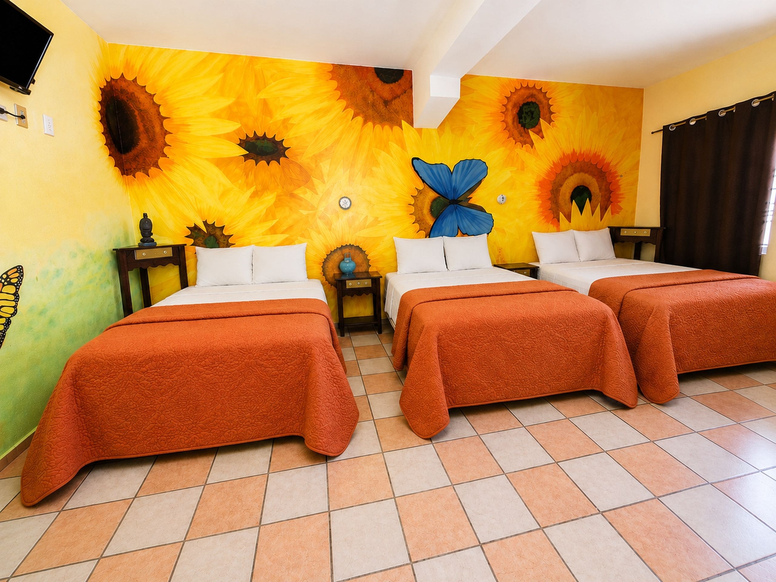 Habitación de hotel con dos camas, un mural grande de girasoles en la pared y piso de baldosas.