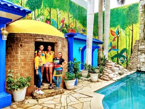 A poolside area with a brick structure, potted plants, and a mural with birds.