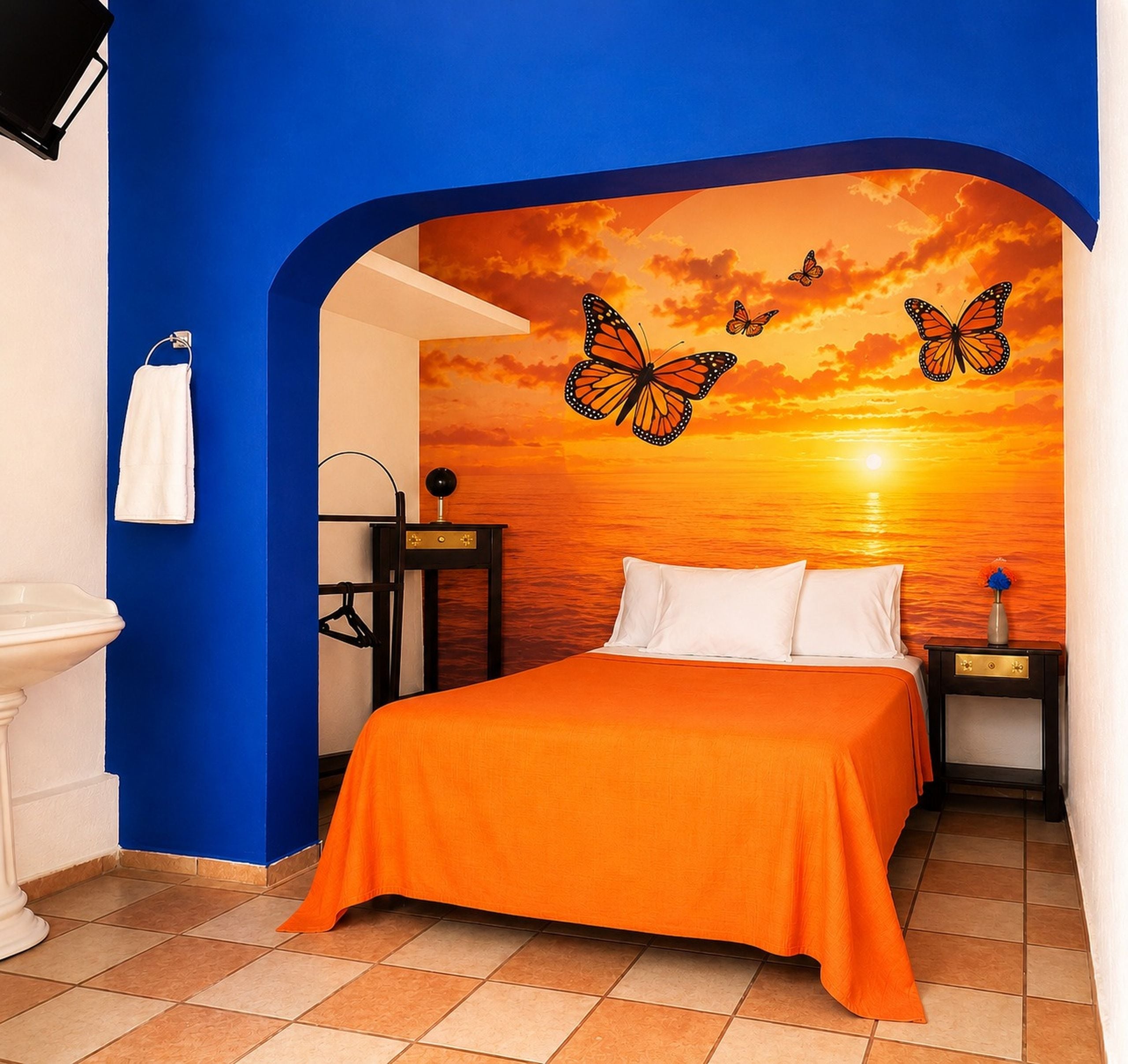 A bedroom with a bed, a nightstand, a wall-mounted shelf, and a bathroom with a sink and towel rack.