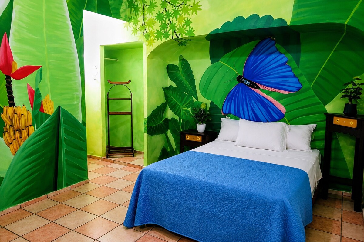 A room with a bed, a nightstand, a plant, and a wall with a large leaf and butterfly mural.