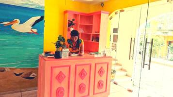 Un mostrador de recepción con una mujer sentada detrás, un mural marino en la pared y una pared de color amarillo brillante.