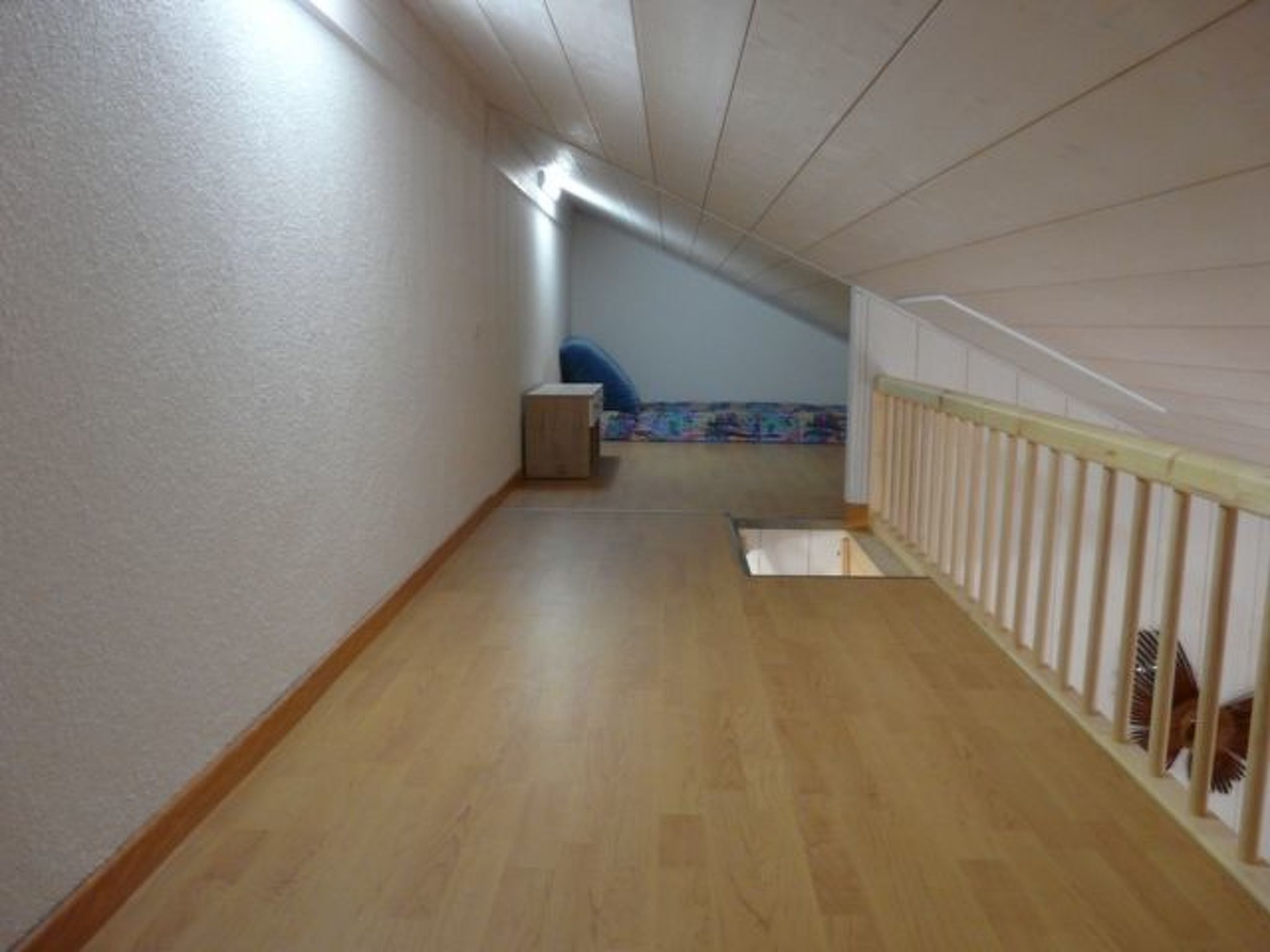 Un estrecho pasillo con suelo de madera, un pequeño cofre y una silla azul.