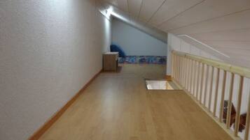 Un couloir étroit avec un plancher en bois, une petite boîte de rangement et une chaise bleue.