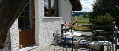 A balcony with a table and chairs, a window, and a view of the countryside.