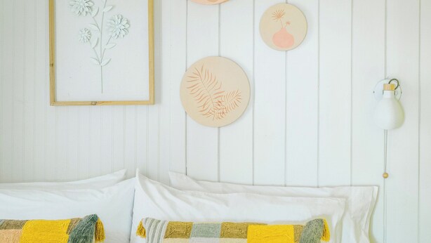 Een slaapkamer met een bed, kussens, een lijst met een kunstwerk en decoraties aan de muur.