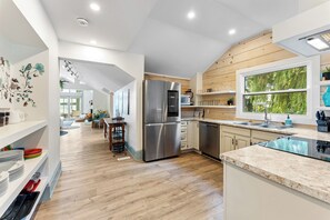 A modern kitchen with a stainless steel refrigerator, wooden cabinets, and a large window offering a view of greenery. - Private Waterfront Retreat! Sunny Lakehouse + 4 Cottages & 10 King Beds (Prince Edward)