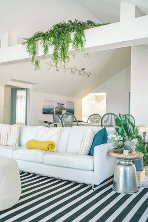 Ein stilvolles Wohnzimmer mit einem weißen Sofa, einem Streifenmuster-Teppich und hängenden Pflanzen.