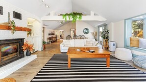 Een ruime woonkamer met een open haard, een bank, een bijzettafeltje en een gestreept vloerkleed.