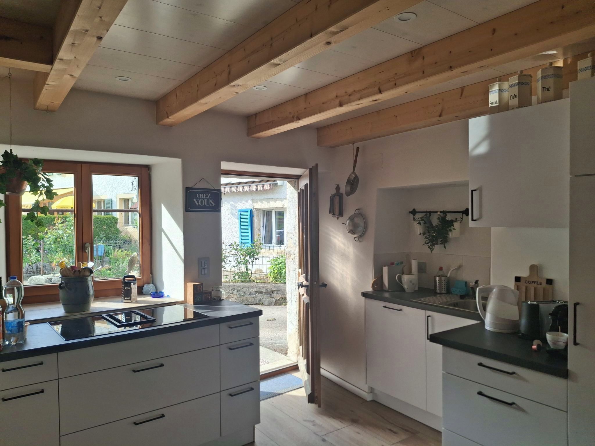 A modern kitchen with white cabinets, a black countertop, and wooden beams on the ceiling.