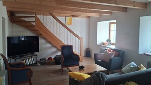 En stue med en trappe i træ, et fladskærms-tv og to lænestole.