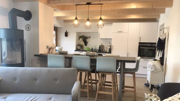 Et moderne køkken med hvide skabe, et spiseområde med lyse stole og en grå sofa.