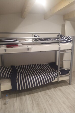 Una cama litera con ropa de cama a rayas, una botella de agua en el suelo y una pared blanca.