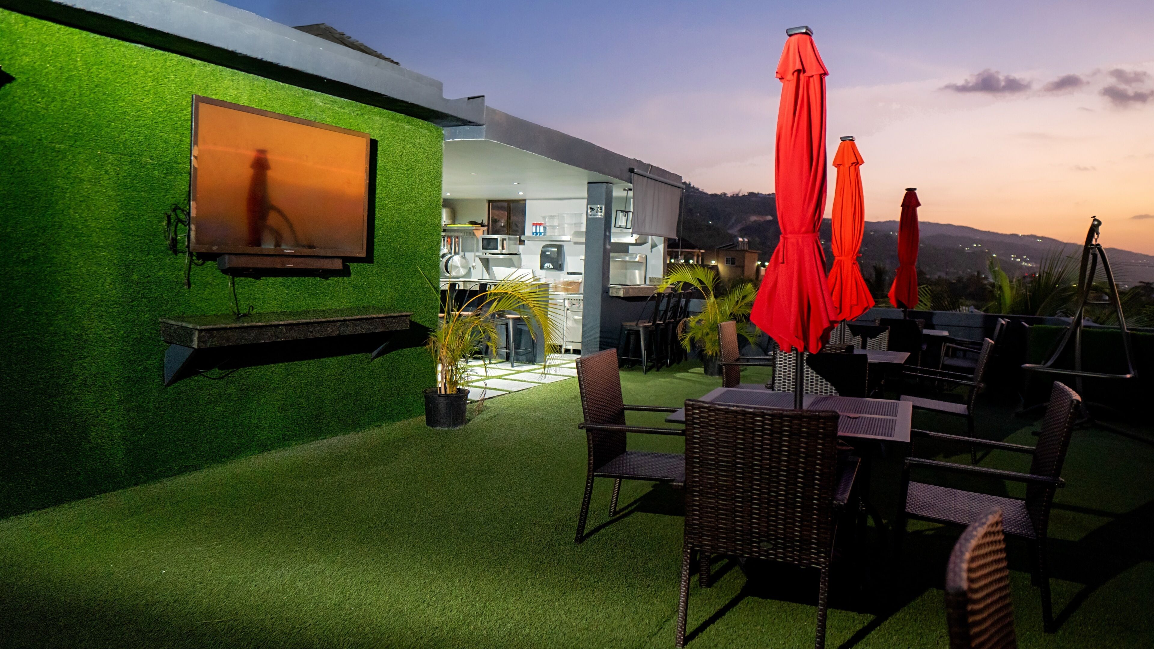 Une terrasse extérieure avec un revêtement de gazon synthétique, des meubles en osier et des parasols rouges.