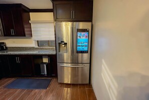 Ein Edelstahl-Kühlschrank mit digitaler Anzeige in einer Küche mit dunklen Holzschränken und einer Granit-Arbeitsplatte.