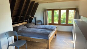 Ein Schlafzimmer mit einem Holzbett, einem Sessel, einem Schreibtisch und einem Fenster mit Vorhängen.