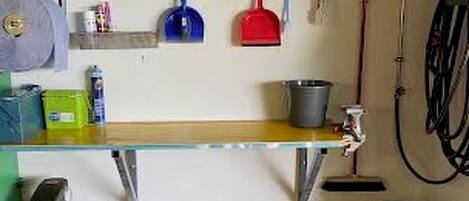 A garage with a workbench, shelves with tools and containers, a green lawnmower, and a hose reel.