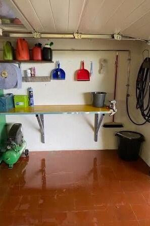 A garage with a workbench, shelves with tools, and a hose.
