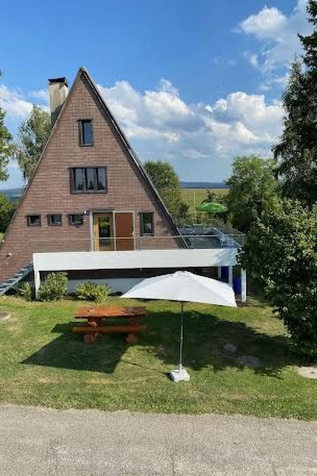 A triangular brick house with a flat roof, a wooden deck, and a white umbrella.
