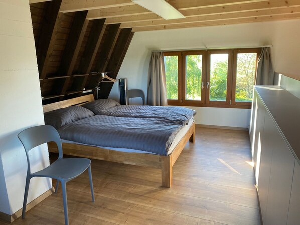 A bedroom with a wooden bed, a chair, a desk, and a window with curtains.