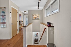 Un couloir étroit avec un plancher en bois, un escalier et une porte donnant sur une autre pièce.