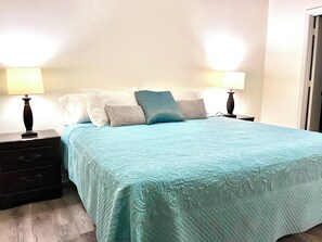 A neatly made bed with a quilted headboard, two bedside tables with lamps, and a wooden nightstand with drawers. - Close Disney! Spacious 3Br 2 Bh Condo / 75" TV, Pool, Parking & No I-4 Traffic! (Kissimmee)