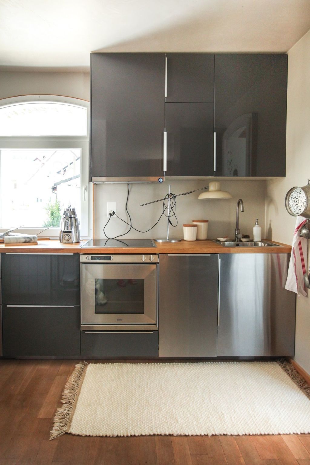 A modern kitchen with stainless steel appliances, a wooden countertop, and a large window.