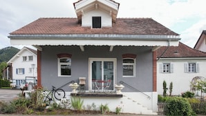 Ein zweistöckiges Haus mit einem Ziegeldach, einer Veranda und einem kleinen Fenster mit dem Schriftzug 'kama'.