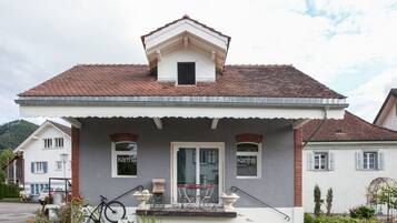 A two-story house with a tiled roof, a front porch with a bicycle, and a small window with the word 'kama' on it.